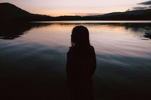 silhouette-di-donna-in-piedi-vicino-al-corso-di-acqua-in-solitudine